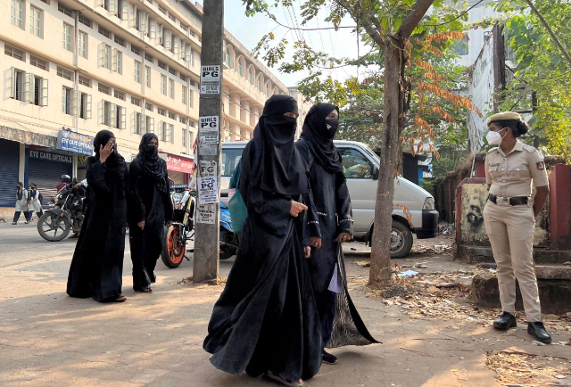 Hijab wearing schoolgirls arrive to attend their classes as a policewoman stands guard outside a government girls school after the recent hijab ban, in Udupi town in the southern state of Karnataka, India, February 16, 2022. REUTERS/Sunil Kataria