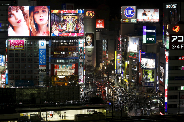 People stand on a platform of the Shibuya train station as digital advertising displays illuminate a junction in central Tokyo, Japan, March 14, 2016. REUTERS/Thomas Peter