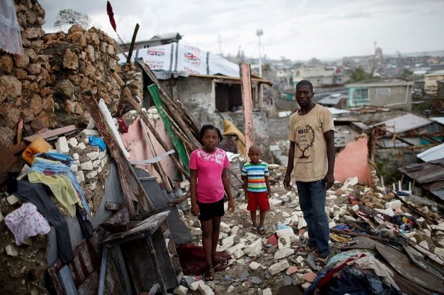 Prenille Nord, 42, poses for a photograph with his children Darline and Kervins among the debris of their destroyed house after Hurricane Matthew hit Jeremie, Haiti, October 17, 2016. REUTERS/Carlos Garcia Rawlins