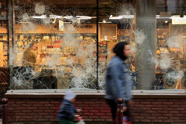 People walk past a shop vandalised during night clashes between protesters and police, following the death of Nahel, a 17-year-old teenager killed by a French police officer in Nanterre during a traffic stop, in Lille, northern France, June 30, 2023