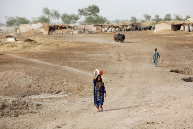 A woman walks to fetch water from a nearby hand-pump with a water cooler on her head, during a heatwave, on the outskirts of Jacobabad, Pakistan, May 16, 2022. REUTERS/Akhtar Soomro