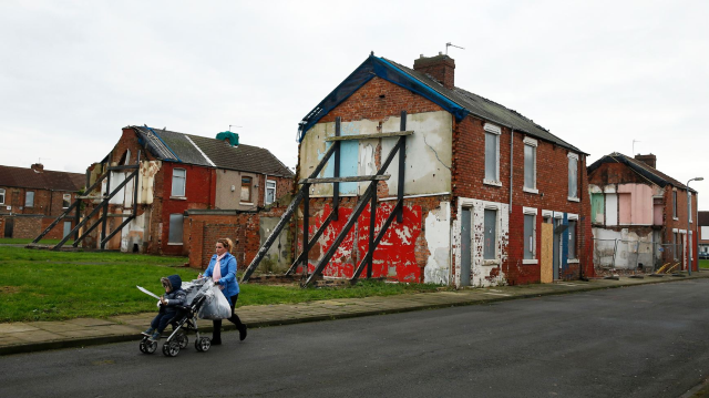 A woman pushes a pram along a semi-derelict terraced street in the Gresham area of Middlesbrough, northern Britain, January 20, 2016. Asylum seekers in the northern English town of Middlesbrough are suffering abuse because they have been housed in properties that almost all have red front doors, making them easy targets for racists. REUTERS/Phil Noble