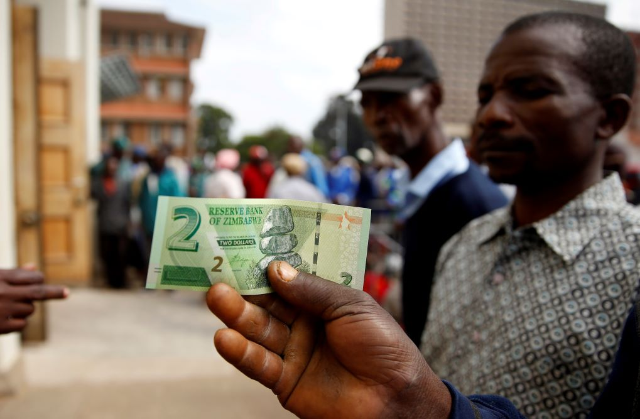 A man poses with Zimbabwe's new two dollar banknote as customers queue outside a bank in Harare, Zimbabwe, November 12, 2019