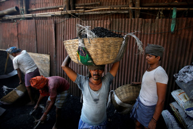 A worker carries a basket filled with coal to load it onto a truck at a coal yard in an industrial area in Mumbai, India, November 30, 2017