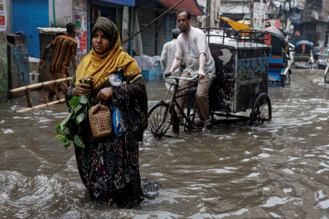 A woman walks along a flooded street after heavy rain, in Dhaka, Bangladesh, June 12, 2023. REUTERS/Mohammad Ponir Hossain