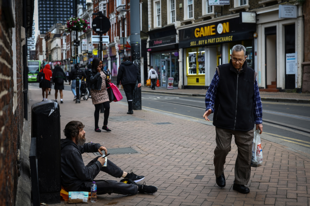 People walk past a man who is homeless on a high street in Croydon, south London, Britain, June 13, 2024. REUTERS/Hannah McKay