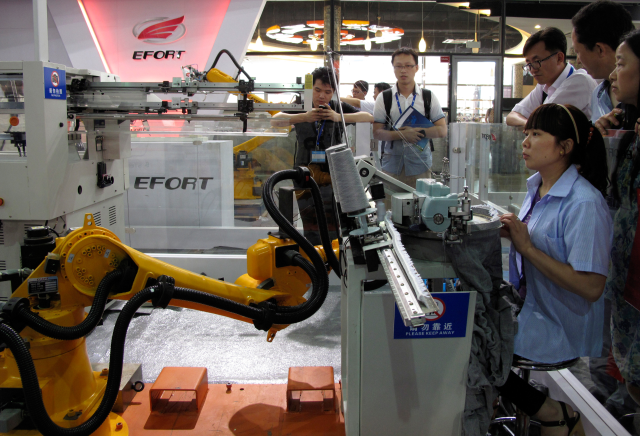 A woman (sitting) races with a textile robot (L) made by domestic manufacturer Anhui Efort at an expo in Shanghai July 10, 2014. REUTERS/Pete Sweeney